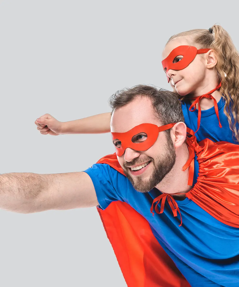 Fliegender Mann im Superman-Kostüm mit einem kleinen Mädchen über ihm liegend und ebenfalls im Superman-Kostüm, beide haben die Faust nach vorne gestreckt